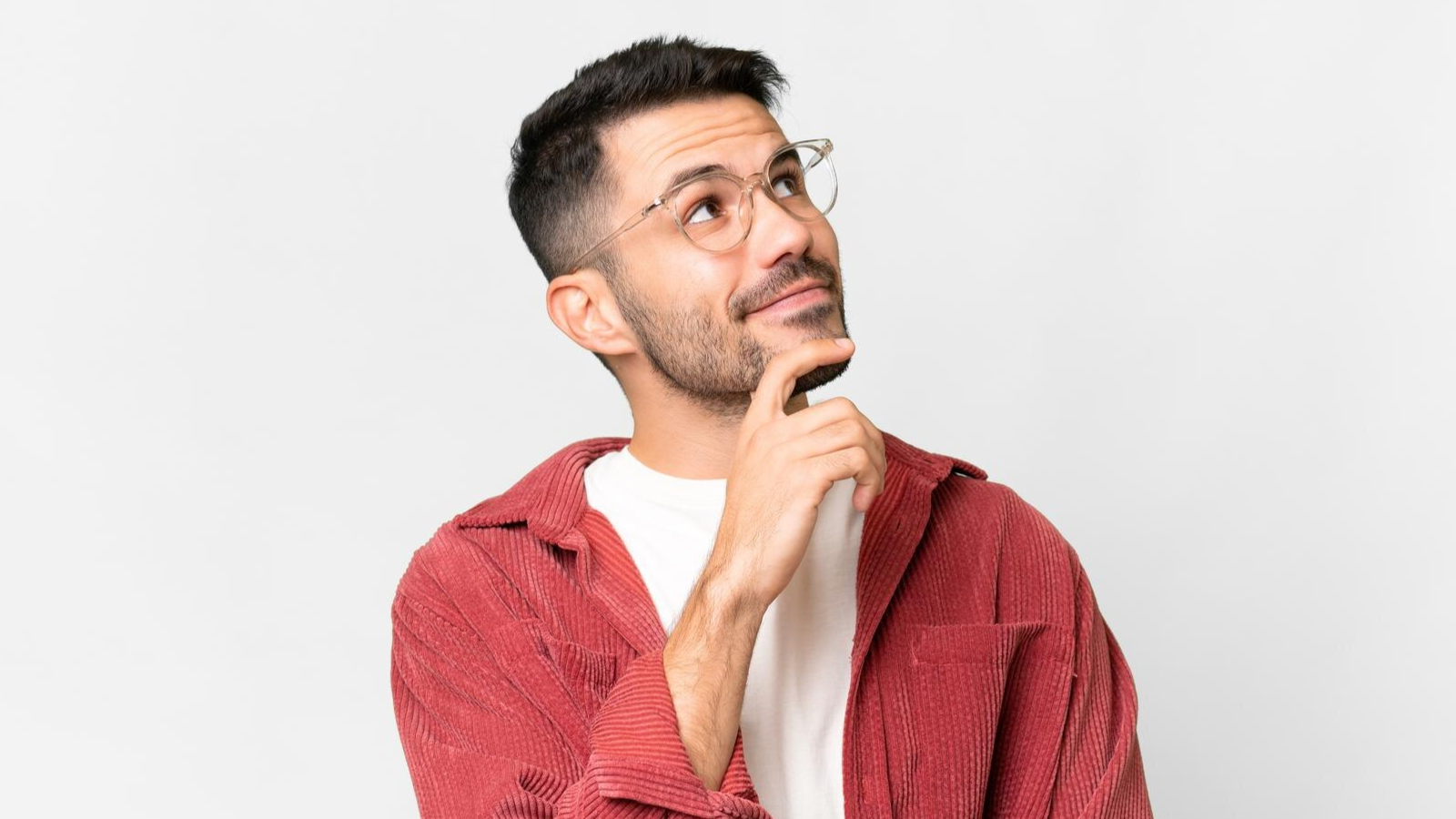 A man wearing glasses and a red jacket looks upward thoughtfully with his hand on his chin, set against a plain white background. This image suggests decision-making or planning, potentially symbolizing business leaders considering hosted PBX or scalable telecom solutions.
