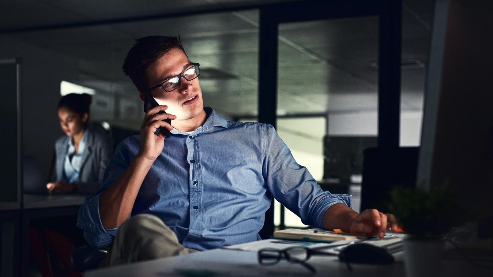Man in an office on a late-night phone call, representing reliable cloud solutions from communications service providers like Nored under any condition.